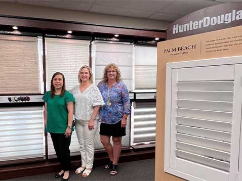 3 women standing in a row next to some window covering samples